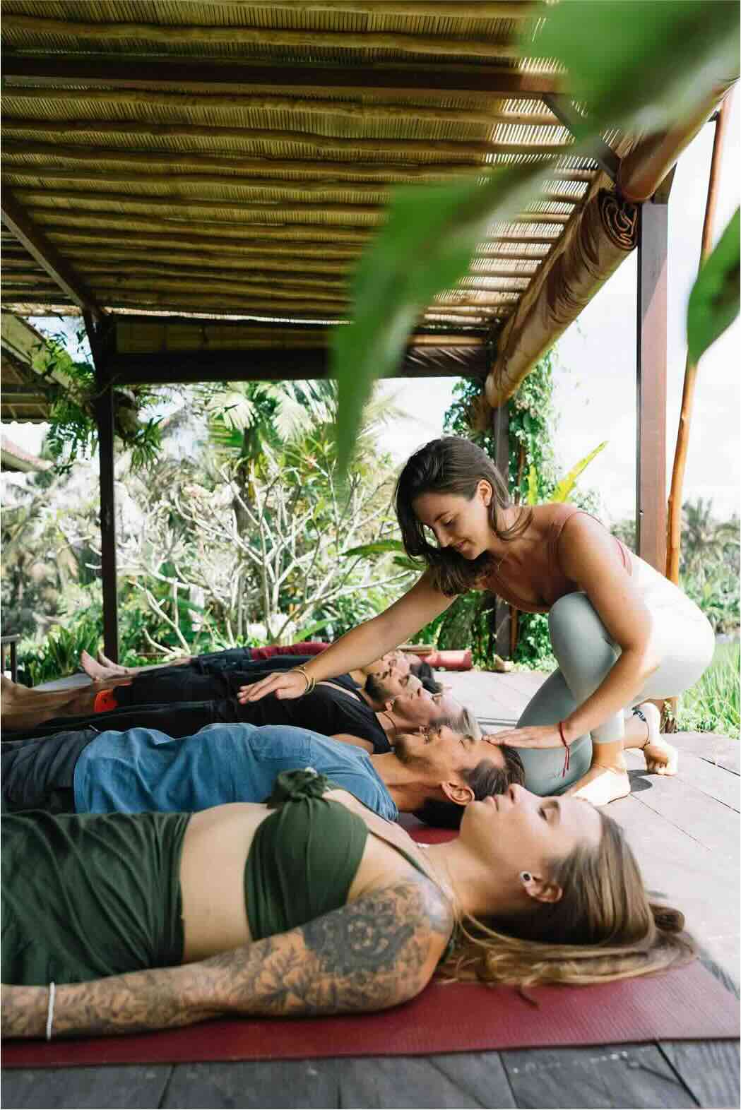 Breathwork facilitator training Bali - participant is learning to aid people with breathwork while they lie on the floor.